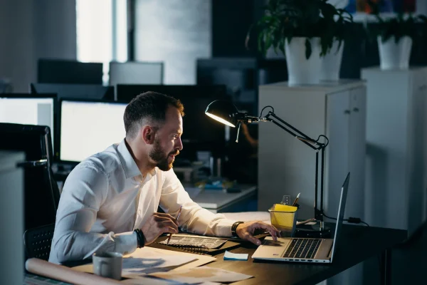 Man has overwork and sitting with laptop and table lamp
