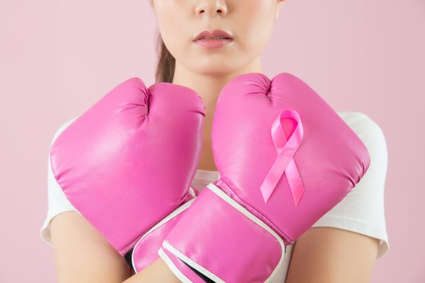 Active Chinese young woman wear boxing gloves crossed arms on the chest to call attention to female cancer disease isolated on pink background. medical and health concept.