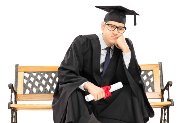Worried college graduate sitting on bench and holding a diploma